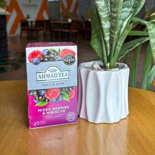 Ahmad Tea Mixed Berries & Hibiscus tea box next to a potted snake plant on a wooden table.